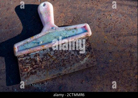 Vecchia spatola in metallo con manico in plastica su un foglio di metallo arrugginito, primo piano, fuoco selettivo Foto Stock