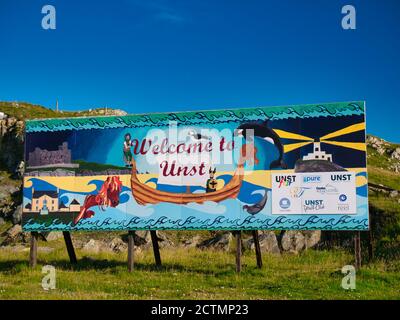 In una giornata di sole con un cielo blu, il cartello Welcome to Unst al terminal dei traghetti di Belmont a sud dell'isola di Unst a Shetland, Scozia, Regno Unito Foto Stock