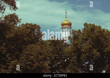 La cupola della chiesa ortodossa sopra gli alberi. Cupola dorata contro il cielo blu. Paesaggio autunnale. Foto Stock