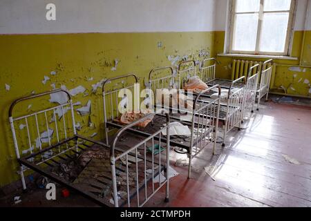 Letti per bambini in un asilo abbandonato. L'interno di un locale in uno degli edifici della zona di esclusione radioattiva di Chernobyl. Foto Stock