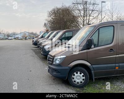 Francoforte, Germania - 25 gennaio 2020: Fila di trasporto marrone consegna Mercedes-Benz Sprinter Electric furgoni essere parcheggiati di fronte alla costruzione di magazzino con cielo drammatico in background - logistica moderna per il settore ecommerce Foto Stock