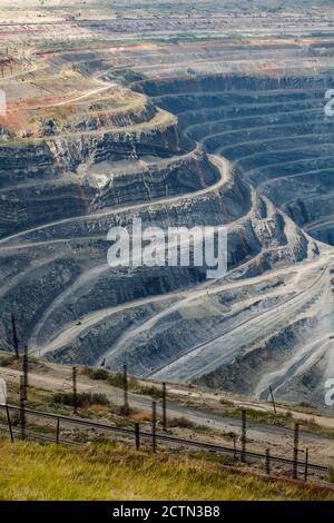 Cava di minerale di ferro gigante a Rudny, Kazakhstan. Minerali grezzi minerari a cielo aperto per la produzione di acciaio. Ferrovia in primo piano. Foto Stock