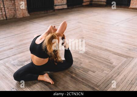 Donna yogini sportiva in forma che fa yoga asana Eka pada kapotasana - posa di piccione a una gamba in stile loft classe Foto Stock