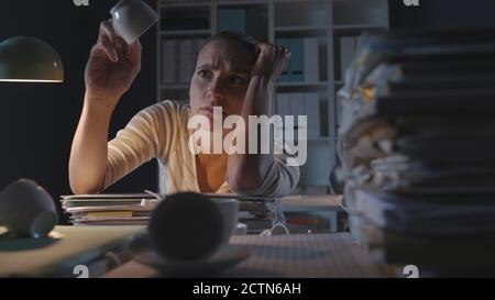 Donna frustrata che lavora in ufficio di notte, ha avuto molte tazze di caffè e si sente esausta, lavorando straordinario concetto Foto Stock