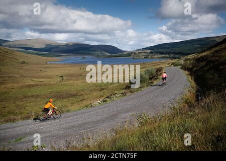 I ciclisti vestiti con colori vivaci si divertono in bicicletta in ghiaia nel Galloway Forest Park, Scozia Foto Stock