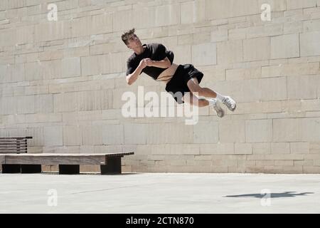Capovolto di giovane maschio che fa il somersault mentre pratica il parkour in zona urbana in estate Foto Stock
