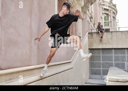 Vista laterale del maschio concentrato che salta sopra la recinzione di pietra e. equilibrio sul braccio durante l'esecuzione di acrobazie e fare parkour Foto Stock