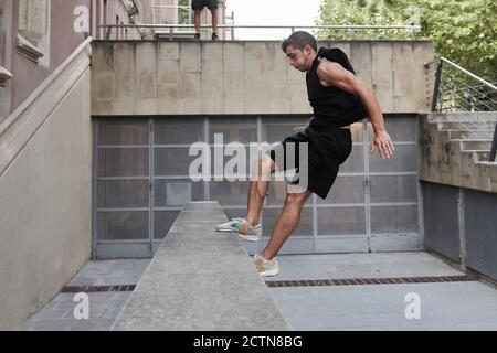 Vista laterale del maschio concentrato che salta sopra la recinzione di pietra mentre eseguire acrobazie e fare parkour Foto Stock