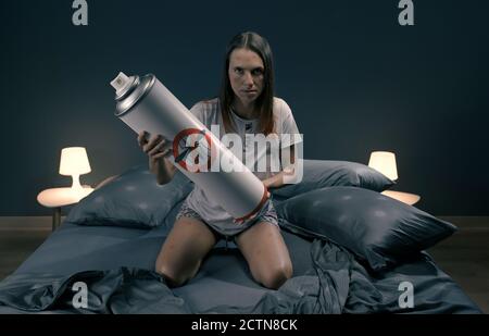 Donna arrabbiata che uccide zanzare nella sua camera da letto di notte utilizzando uno spray repellente per insetti Foto Stock