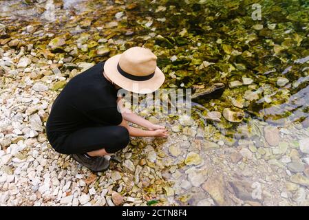 Dall'alto del turista femminile bere acqua chiara da calma fiume nella foresta durante l'avventura estiva Foto Stock