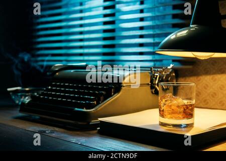 Desktop di scrittore in stile noir con macchina da scrivere e un bicchiere di whisky, creatività e ispirazione Foto Stock