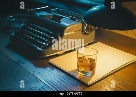 Desktop di scrittore in stile noir con macchina da scrivere e un bicchiere di whisky, creatività e ispirazione Foto Stock