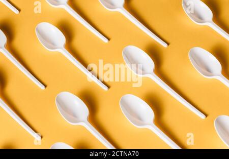 Vista dall'alto piatto composizione di cucchiai monouso in plastica bianca per cibo da asporto disposto su sfondo giallo Foto Stock