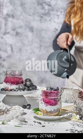 Vasetto di vetro con yogurt nutriente con sana muesli e fresco mirtilli messi a tavola per la colazione al mattino Foto Stock