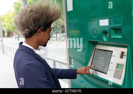 Vista laterale del giovane africano con trazione dei capelli fuori un biglietto sul tram che indossa una cuffia senza fili intorno al collo Foto Stock