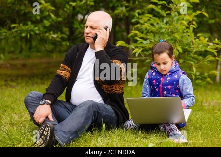 Sorridi un nonno elegante e attraente utilizzando uno smartphone, una nipote che utilizza un computer portatile. Utilizzando la tecnologia di social network Internet con l'orologio digitale Foto Stock