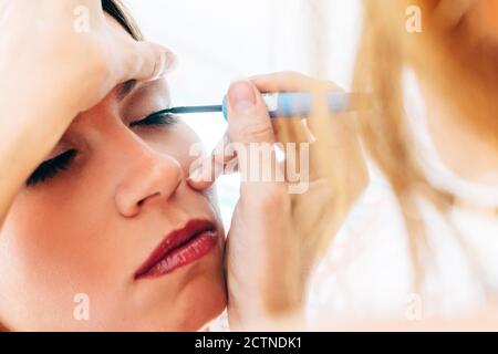anonimo donna trucco artista applicando eyeliner sul modello calmo in luminoso studio di bellezza Foto Stock