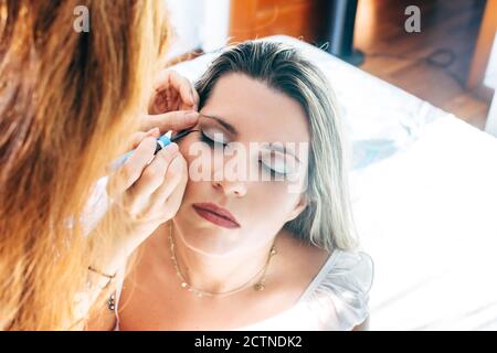 anonimo donna trucco artista applicando eyeliner sul modello calmo in luminoso studio di bellezza Foto Stock