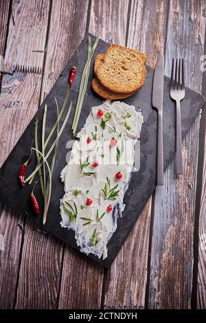 Dall'alto di gustoso formaggio cremoso e pezzi di fresco pane arrangiato con varie erbe su tavola di ardesia su legno tabella Foto Stock