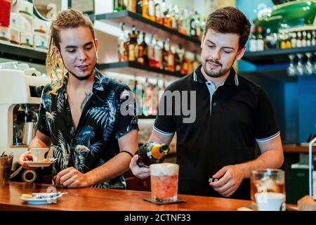 Barman serve una tazza di caffè fresco e un bicchiere di freddo cocktail con cubetti di ghiaccio mentre ci si trova al bancone del bar Foto Stock