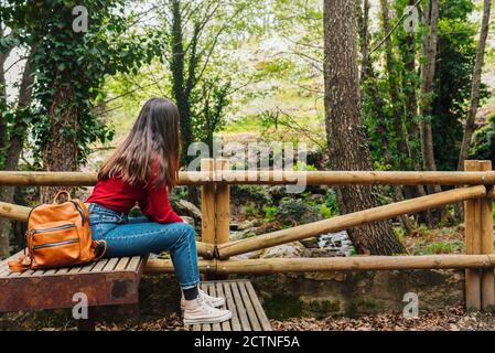 Vista laterale di una donna anonima turista seduto su una vecchia panca In boschi e ammirando la magnifica natura in Valle del Jerte Foto Stock