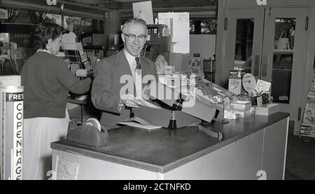 Anni '50, storico, in un negozio di mom-and-pop o generale, al banco del negozio, il proprietario mostrando una scatola contenente cartelle di 'Krystaltone' stampe fotografiche che è stato appena consegnato, Oregon, Stati Uniti. Foto Stock