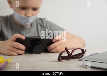 un ragazzo in una t-shirt grigia si siede a un portatile ed è impegnato in linea, messa a fuoco in primo piano, a distanza di apprendimento, un ragazzo a un portatile a un tavolo stampa Foto Stock