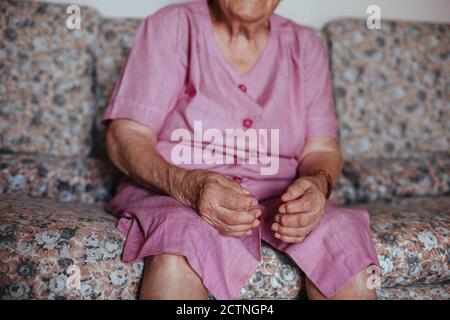 Vista frontale di una donna anziana irriconoscibile con problemi di salute mentale di Alzheimer seduto in un divano da solo nella sua casa Foto Stock