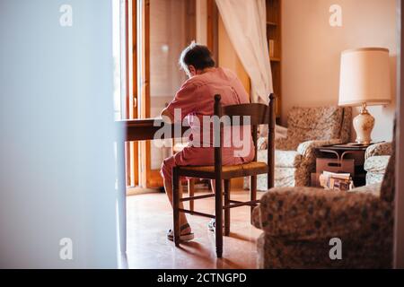 Vista posteriore di una donna anziana con problemi di salute mentale di Alzheimer dipingere su un notebook all'interno della sua casa Foto Stock