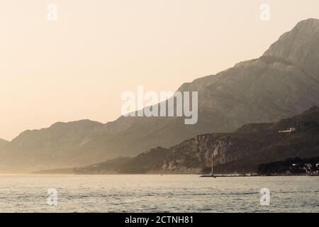 Spettacolare scenario di mare vicino a montagne rocciose sotto il cielo rosa In mattinata nebbia in Croazia Foto Stock