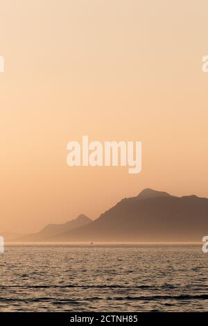 Spettacolare scenario di mare vicino a montagne rocciose sotto il cielo arancione In mattinata nebbia in Croazia Foto Stock