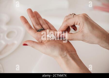 anonimo artigianale femminile che crea petalo di fiore da morbido plymer argilla in uno studio luminoso mentre si utilizza un attrezzo speciale Foto Stock