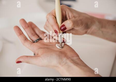 anonimo artigianale femminile che crea petalo di fiore da morbido plymer argilla in uno studio luminoso mentre si utilizza un attrezzo speciale Foto Stock