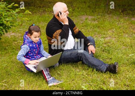 Sorridi un nonno elegante e attraente utilizzando uno smartphone, una nipote che utilizza un computer portatile. Utilizzando la tecnologia di social network Internet con l'orologio digitale Foto Stock