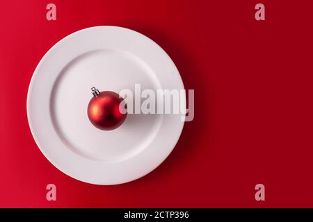 Palla di Natale e piatto bianco su sfondo rosso. Cena di Natale. Foto Stock