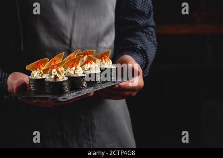 Sushi roll maki futo cibo giapponese su un piatto di pietra nera nelle mani di un cameriere. Primo piano Foto Stock