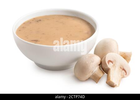 Crema di zuppa di funghi in una ciotola bianca in ceramica accanto ai funghi freschi a bottoni isolati su bianco. Nessuna modanatura. Foto Stock
