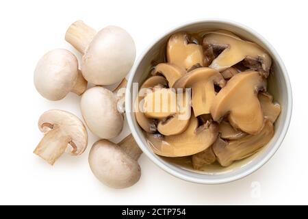 Funghi a bottoni tagliati in scatola in una ciotola bianca in ceramica accanto ai funghi freschi a bottoni isolati su bianco. Vista dall'alto. Foto Stock