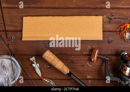 Diverse tegole da pesca con esche e bobine su sfondo marrone di legno con posto per il testo. Design per la pubblicità e la pubblicazione. Foto Stock