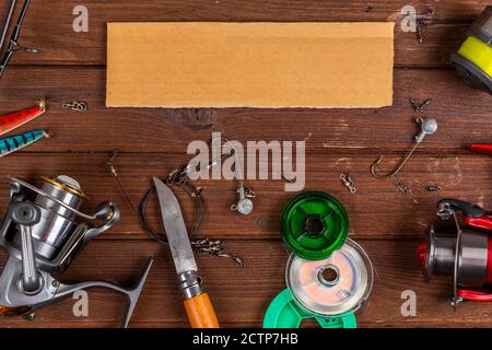 Diverse tegole da pesca con esche e bobine su sfondo marrone di legno con posto per il testo. Design per la pubblicità e la pubblicazione. Foto Stock