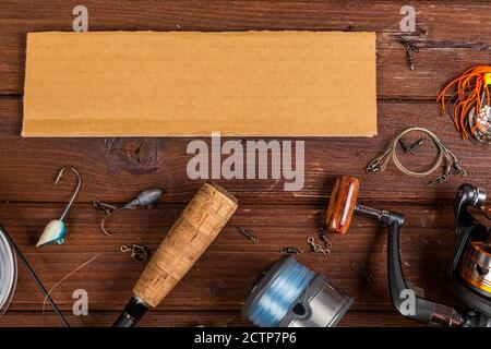 Diverse tegole da pesca con esche e bobine su sfondo marrone di legno con posto per il testo. Design per la pubblicità e la pubblicazione. Foto Stock