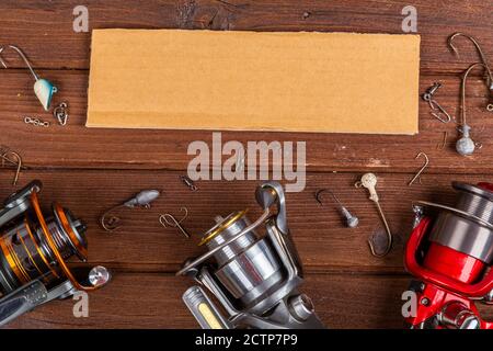 Diverse tegole da pesca con esche e bobine su sfondo marrone di legno con posto per il testo. Design per la pubblicità e la pubblicazione. Foto Stock