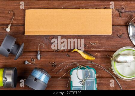 Diverse tegole da pesca con esche e bobine su sfondo marrone di legno con posto per il testo. Design per la pubblicità e la pubblicazione. Foto Stock