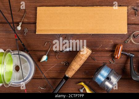 Diverse tegole da pesca con esche e bobine su sfondo marrone di legno con posto per il testo. Design per la pubblicità e la pubblicazione. Foto Stock