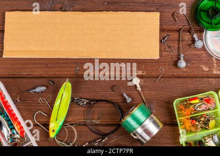Diverse tegole da pesca con esche e bobine su sfondo marrone di legno con posto per il testo. Design per la pubblicità e la pubblicazione. Foto Stock