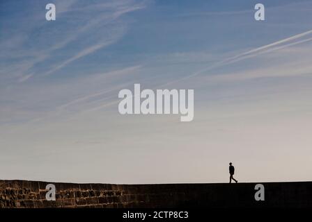 Persona in silhouette che cammina lungo il Cobb a Lyme Regis in Dorset, Inghilterra Foto Stock