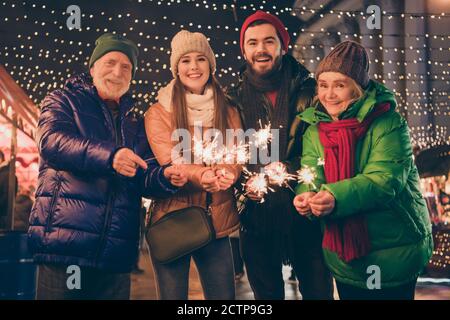 Foto della famiglia piena quattro membri x-mas riunione tenere bengala fire wait babbo natale presenta cappellino tradizionale per eventi cappotto di sciarpa sera Foto Stock