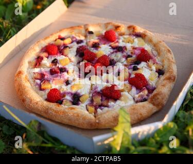 Pizza di frutta con lamponi, mirtilli e pezzetti di ananas. Una scatola di pizza al picnic Foto Stock