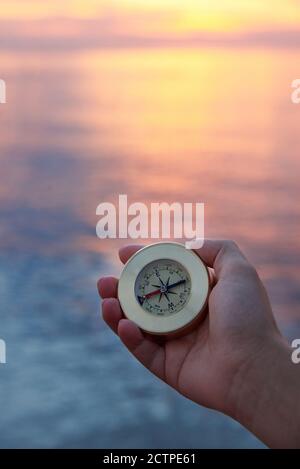 Mano della donna con una bussola sulla costa del mare all'alba. Concetto di viaggio. Foto Stock
