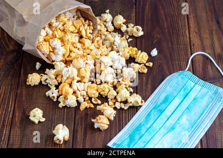 Una ciotola trasparente di popcorn su una superficie di legno. Accanto a un computer portatile e alle cuffie. La maschera protegge dai virus. Spazio di copia. Foto Stock